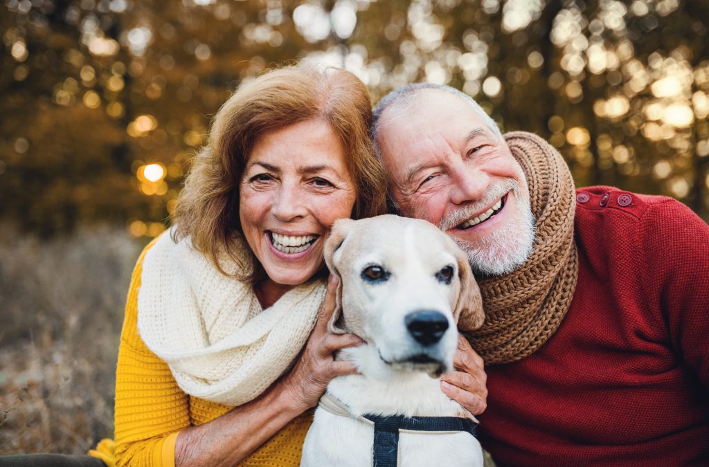 A retired couple taking their dog for a walk in the fall.